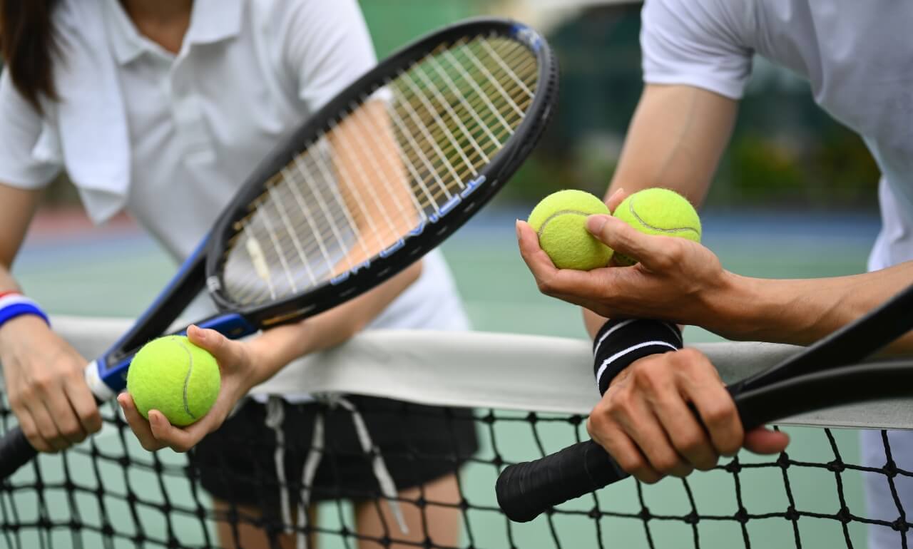 cropped photo of tennis players at the net holding rackets and balls